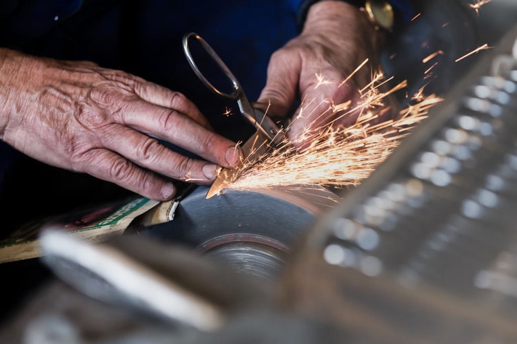 A craftsman grinding a scissor blade, sparks flying, in the Sheffield workshop